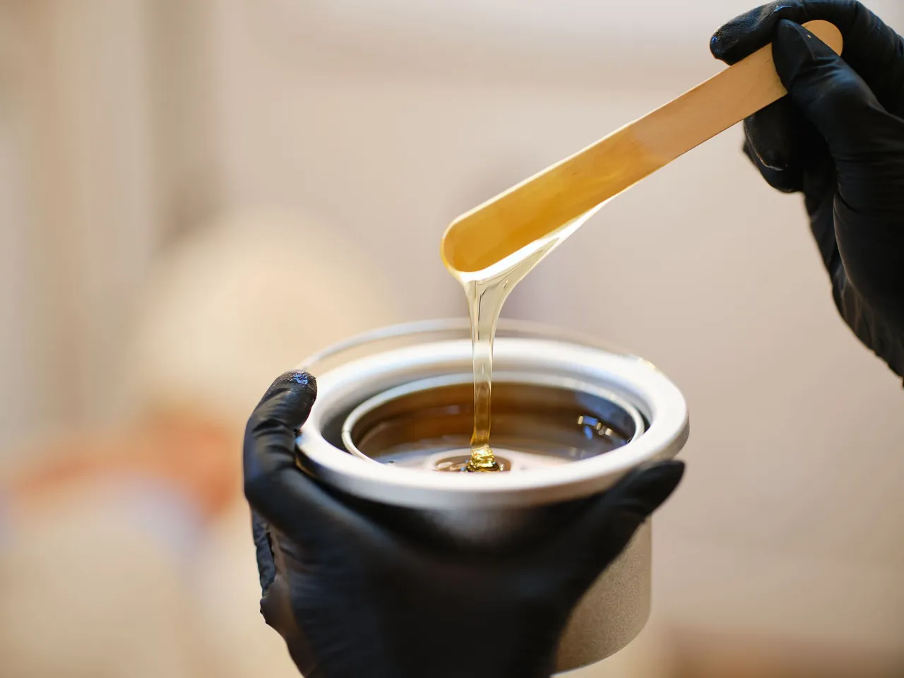 Warm wax dripping from a wooden spatula over the wax pot
