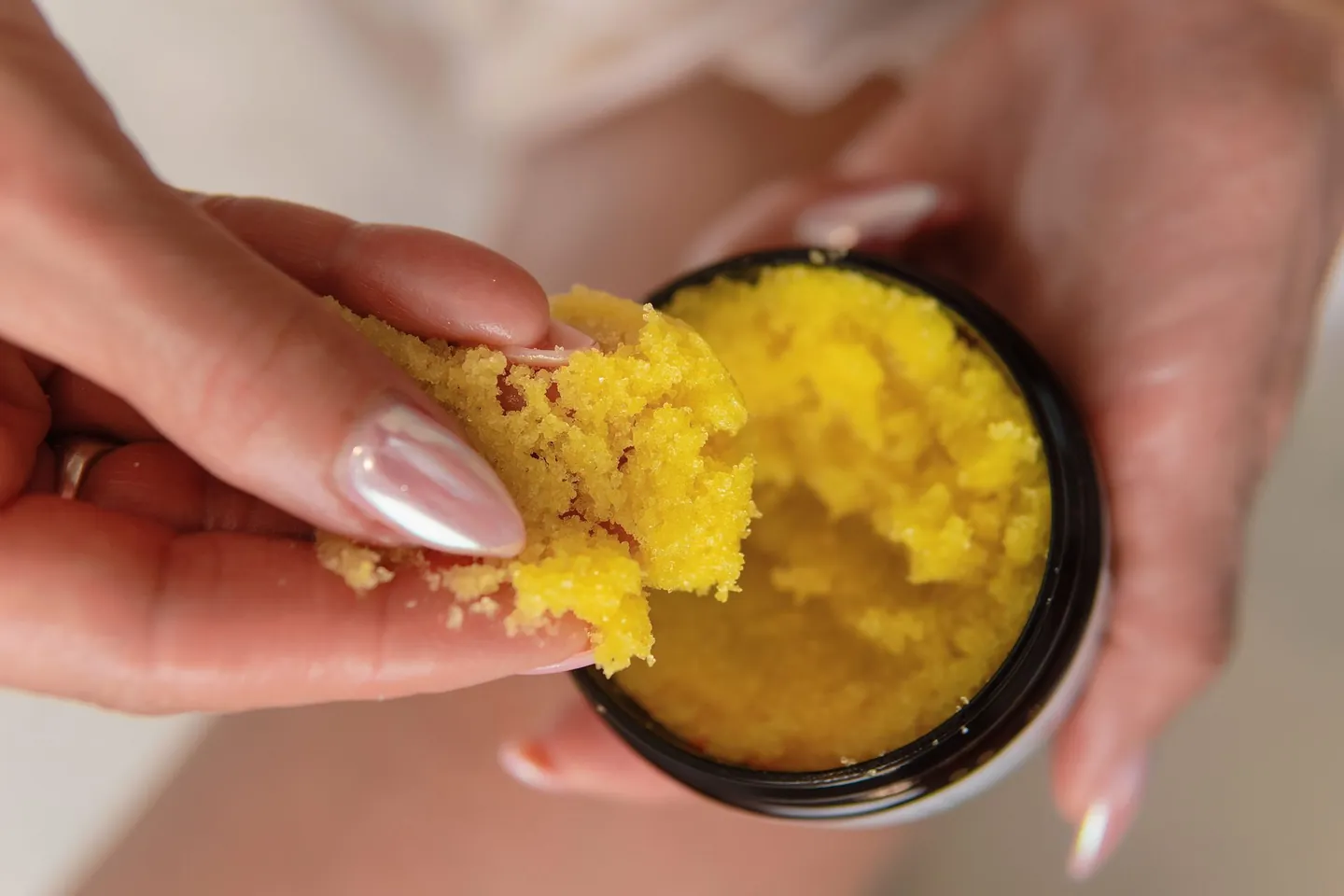 A hand scooping Stay Smooth Body Bright Scrub from the jar